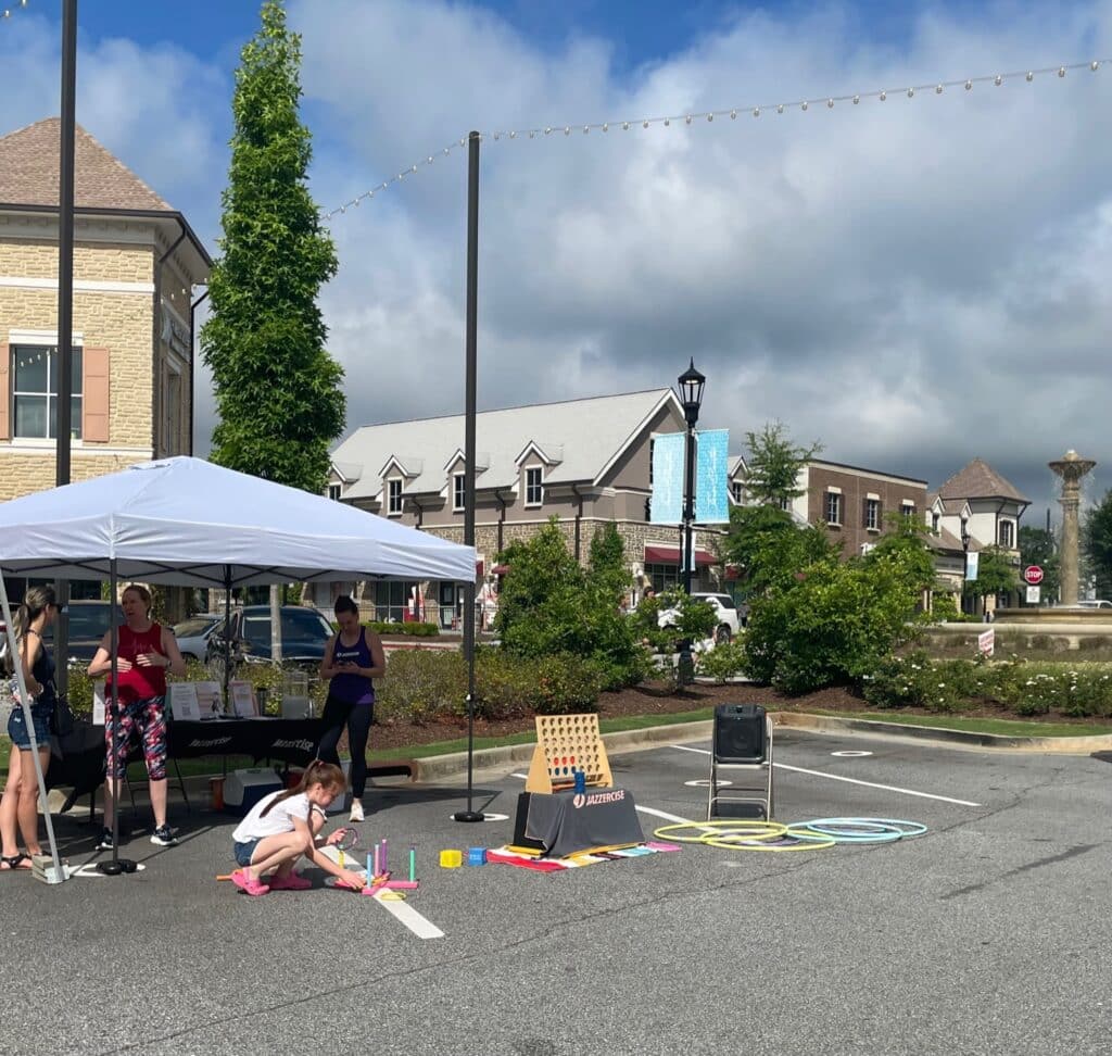 A young girl is crouched next to a row of outdoor games at a farmers market booth
