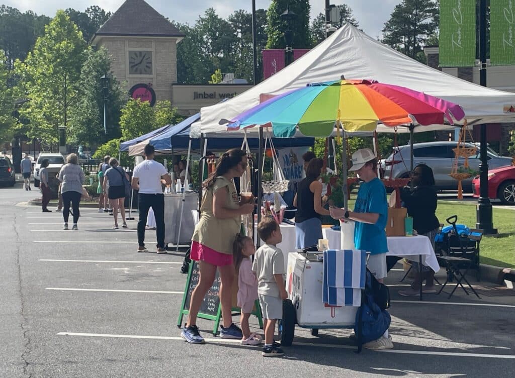 A king of pops cart with rainbow umbrella at an outdoor farmers market.