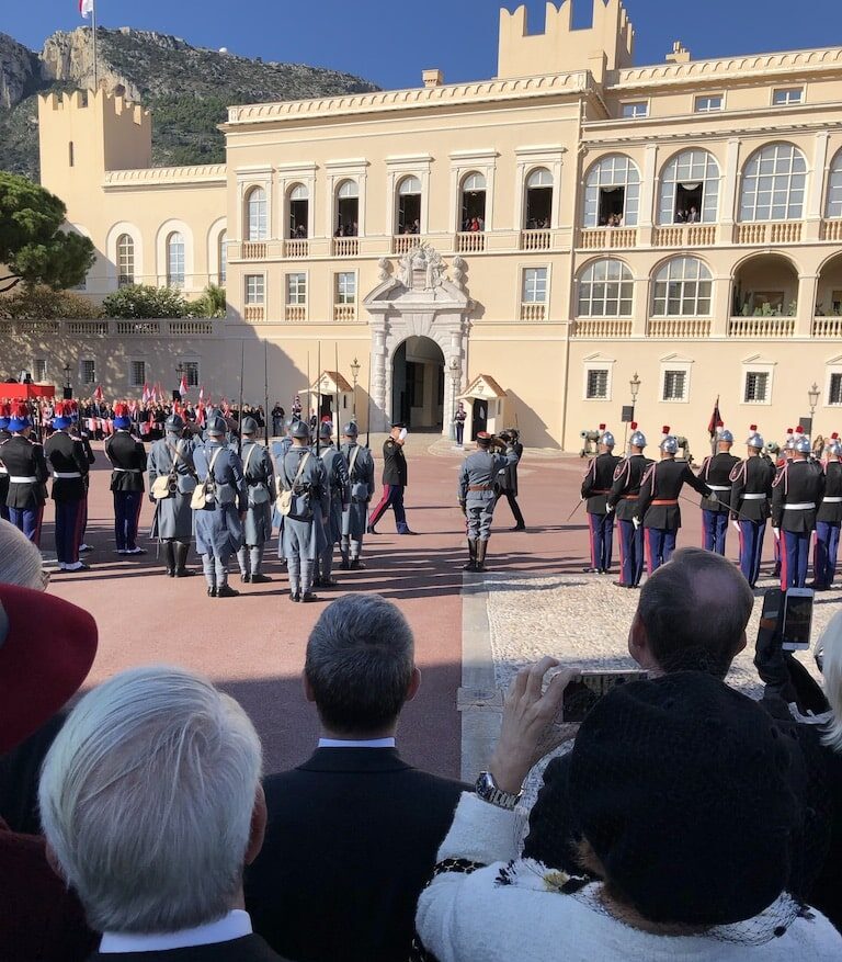 Royal guard in Monaco. People are standing around watching them in an outdoor courtyard in front of an historic building.