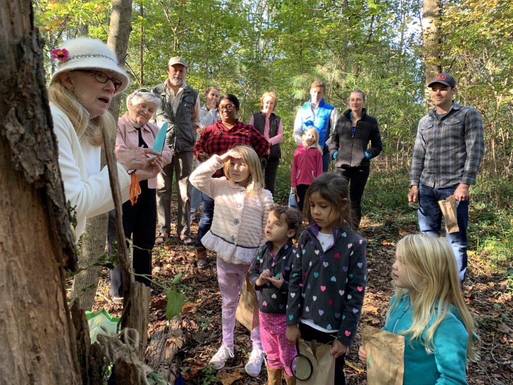 A group of kids and adults in the woods for a nature class.