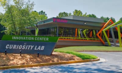 Exterior of the Curiosity Lab campus in Peachtree Corners. There's a building with T-Mobile signage, and entrance sign that reads "Innovation Center Curiosity Lab" and a small parking lot surrounded by grass and trees.