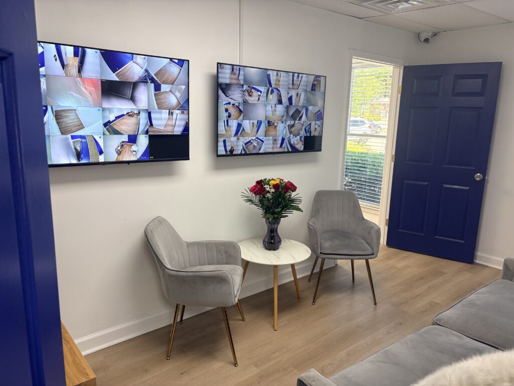 An empty waiting room area at the Success on the Spectrum location in Peachtree Corners. There are two chairs, a small side table, a sofa and two flat screen monitors on the wall.